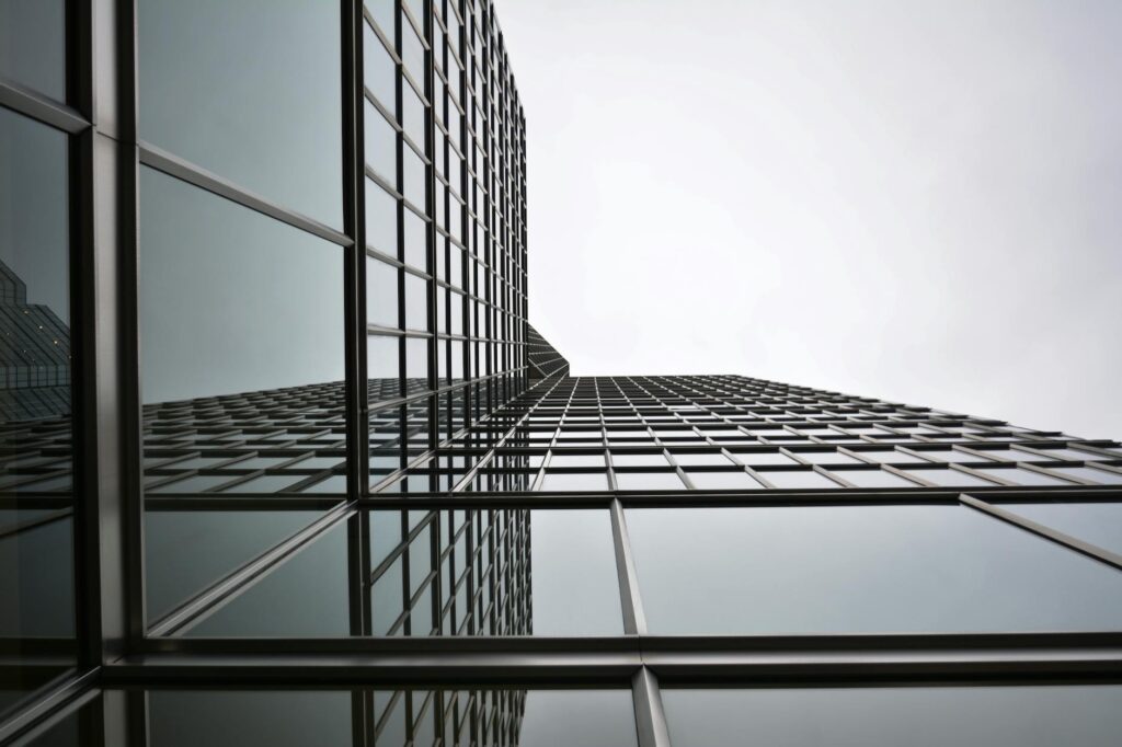 Low angle view of a modern glass skyscraper with reflective panels in an urban setting.