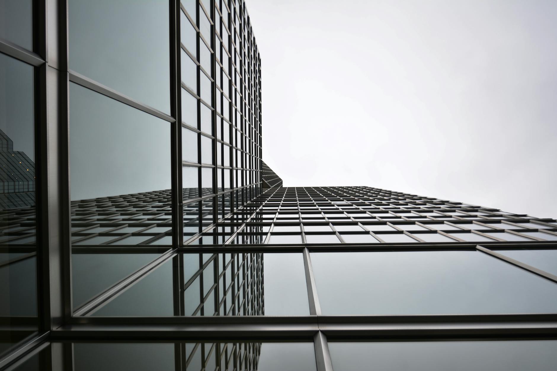 Low angle view of a modern glass skyscraper with reflective panels in an urban setting.